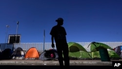 A migrant from Honduras seeking asylum in the United States stands in front of rows of tents at the border crossing, Monday, March 1, 2021, in Tijuana, Mexico. 