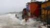 An Indian man stands on shore as waves caused by high tide hit the huts on the shore of Arabian Sea in Mumbai, India, Wednesday, July 3, 2019. 