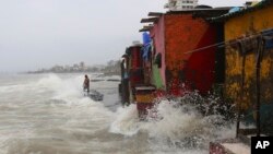 An Indian man stands on shore as waves caused by high tide hit the huts on the shore of Arabian Sea in Mumbai, India, Wednesday, July 3, 2019.