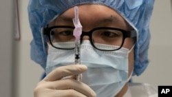 A pharmacist poses with a syringe in a clean room where doses of COVID-19 vaccines will be loaded into syringes, Dec. 9, 2020, at Mount Sinai Queens hospital in New York.
