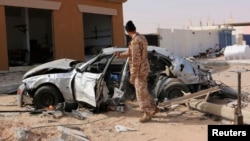 A Libyan soldier allied with the self-proclaimed Tripoli government stands next to a damaged vehicle at the scene of an air attack in Ben Jawad, Feb. 2, 2015.