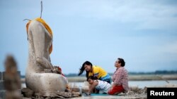 A family prays near the ruins of a headless Buddha statue, which has resurfaced in a dried-up dam due to drought, in Lopburi, Thailand, Aug. 1, 2019.