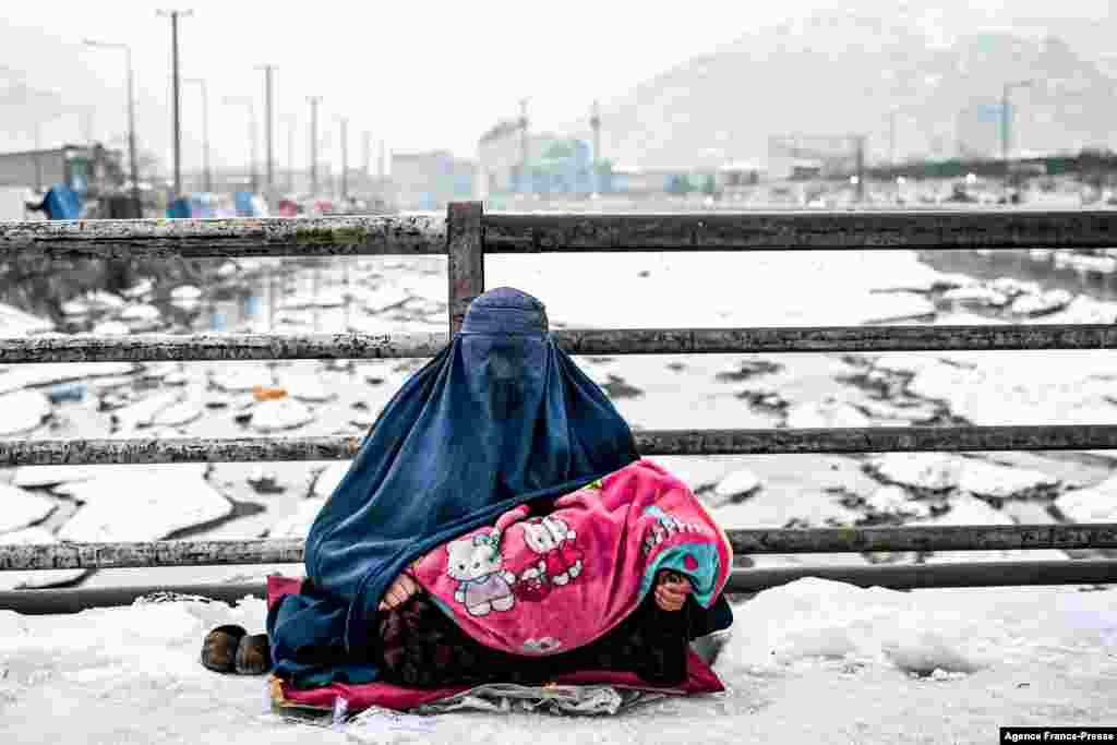 An Afghan woman sits with a child as she seeks donations from people walking past her on a bridge covered with snow in Kabul.