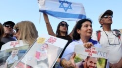 Orang-orang membawa poster yang memuat gambar sandera Israel yang baru dibebaskan, Yarden Bibas, serta kedua anaknya, Kfir dan Ariel, saat mereka menonton pembebasan sandera Israel di Jalur Gaza di layar di lapangan sandera di Tel Aviv pada 1 Februari 2025. (Foto: AFP)