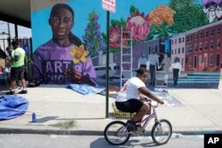A boy rides his bicycle, July 29. 2019, after volunteering to paint a mural outside the New Song Community Church in the Sandtown section of Baltimore.