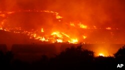 A wildfire burns on a hillside above stopped railcars near Othello, Wash., early Sunday, Aug. 13, 2017.