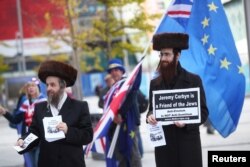 FILE - Two men wearing Orthodox Jewish attire hold placards and leaflets in support of Labor Party leader Jeremy Corbyn outside the party's conference in Liverpool, England, Sept. 26, 2018.
