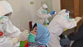 A health worker collects nasal swab samples from a woman during a mass test for the new coronavirus in a neighborhood in Tangerang, Indonesia, July 17, 2020.