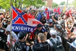 FILE- Members of the white supremacist KKK are escorted by police past a large group of protesters during a KKK rally in Charlottesville, Va., July 8, 2017.