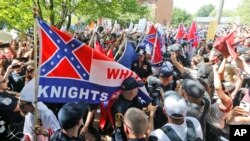 FILE- Members of the white supremacist KKK are escorted by police past a large group of protesters during a KKK rally in Charlottesville, Virginia, July 8, 2017.