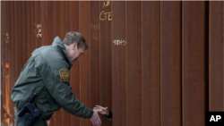Esta fotografía del 15 de enero de 2019 muestra a Rodney Scott, jefe del sector de San Diego de la Patrulla Fronteriza, estrechando la mano a otra persona a través de una sección del muro fronterizo, en San Diego.
