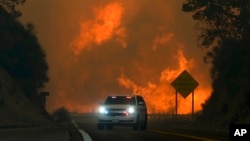 FILE - The Line Fire jumps Highway 330 as an emergency vehicle is driven past, near Running Springs, California, Sept. 7, 2024.