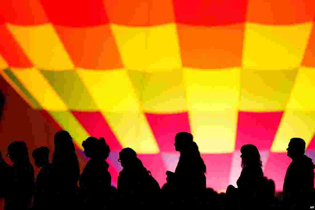 People are silhouetted against a hot air balloon during a balloon glow as part of Memorial Day weekend activities on the grounds of the National World War I Museum and Memorial, Sunday, May 30, 2021, in Kansas City, Mo. (AP Photo/Charlie Riedel)