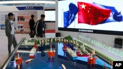 FILE - Visitors look at models of tanker-shaped floating nuclear reactors and oil rigs showcased at the China International Exhibition on Nuclear Power Industry in Beijing on April 27, 2017. China is developing floating nuclear reactors for the South China Sea.