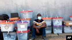 A polling agent sits next to ballot boxes as vote counting continues at various stations in Lusaka, Zambia, Aug. 13, 2021. 