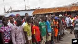 West Point residents stand behind a green string marking a holding area, as they wait for a second consignment of food from the Liberian Government to be handed out, at the West Point area, near the central city area of Monrovia, Liberia, Friday, Aug. 22,