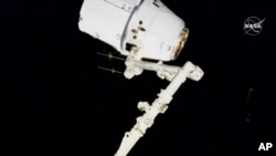 FILE - In this image taken from NASA video, astronauts Andrew Morgan and Jessica Meir use the International Space Station's robot arm to capture the Dragon capsule on March 9, 2020. 