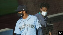 Seattle Mariners' Mallex Smith, left, and Dee Gordon, right, wear masks as they enter the dugout, July 20, 2020, during a "summer camp" baseball scrimmage game in Seattle. 