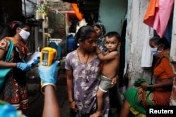 A healthcare worker checks the temperature of residents of a slum area using an electronic thermometer, in Mumbai, India, July 6, 2020.
