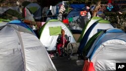 FILE - A woman refugee sits on a wheelchair among tents at the port of Piraeus, near Athens, Greece, April 9, 2016. 