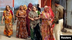 A policeman checks identity papers of women as they arrive to cast their votes at a polling station during the first phase of Gujarat state assembly election in Panshina village of Surendranagar district, Dec. 9, 2017.