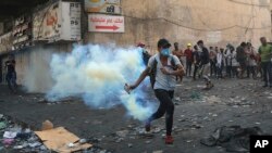 An anti-government protester prepares to throw back a tear gas canister fired by police during clashes between Iraqi security forces and demonstrators, in downtown Baghdad, Iraq, Nov. 13, 2019. 