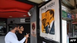 Des Tunisiens regardent une affiche du film "Papa Hedi, l'homme au microphone" dédiée au grand chanteur tunisien Hedi Jouini et réalisée par sa petite-fille Claire, à Tunis, le 23 octobre 2018.