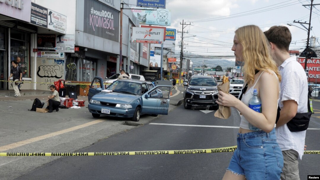 Turistas caminan cerca del lugar donde asaltantes dispararon e hirieron a dos personas que viajaban en un vehículo en la capital San José, el 10 de enero de 2024.