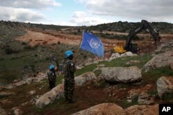 Pasukan penjaga perdamaian PBB mengibarkan bendera mereka, saat mengamati ekskavator Israel berupaya menghancurkan terowongan yang dibangun oleh Hizbullah, dekat perbatasan Lebanon-Israel selatan, Mays al-Jabal, Lebanon, 13 Desember 2019. (Foto: AP)