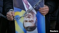 FILE - A protester holds an upturned poster of Ukrainian President Viktor Yanukovych during a rally in Kyiv, Dec. 26, 2013.