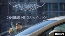 A woman cleans the window at a Aston Martin luxury car dealership in Beijing, Dec. 12, 2018. Auto sales have fallen sharply in China.