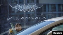 A woman cleans the window at a Aston Martin luxury car dealership in Beijing, Dec. 12, 2018. 