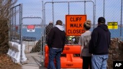 Visitors look through a barrier placed around a collapsed part of the historic Cliff Walk on March 15, 2022 in Newport, Rhode Island. (AP Photo/Charles Krupa)