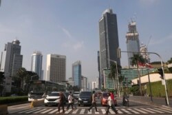 Orang-orang yang memakai masker wajah menyeberang jalan di kawasan bisnis utama di Jakarta yang terlihat sepi, Senin, 8 Juni 2020. (Foto: AP)