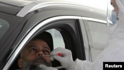 FILE - A health worker collects a sample at a drive-through COVID-19 screening center at the Ain Shams field hospital, in Cairo, Egypt, June 15, 2020.