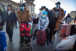 Travelers wear face masks as they walk outside of the Beijing Railway Station in Beijing, Jan. 20, 2020.
