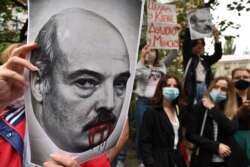 A member of the Belarus diaspora holds a placard depicting Alexander Lukashenko with blood on his mouth during a rally outside the Belarusian embassy in Kyiv, Aug. 13, 2020.