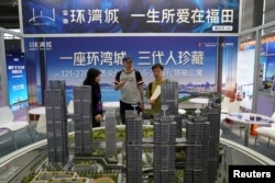 Seorang agen melayani pelanggan di dekat model skala bangunan tempat tinggal di pameran properti di Shenzhen, Provinsi Guangdong, China, 12 Oktober 2024. (Foto: REUTERS/Nicoco Chan)