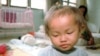 A young orphaned Cambodian infant girl infected with the HIV virus sits on a mat in the Phnom Penh Nutrition Center.