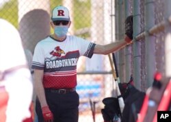 FILE - John Journey, 86, wearing a mask to the prevent the spread of COVID-19, listens to his team coach speak in the dugout before a 65-and-over league softball game, April 20, 2021, in Richardson, Texas.