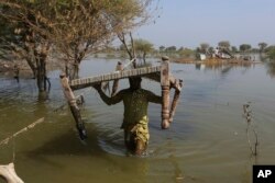 FILE - Villagers retrieve belongings, which were they kept on the higher ground surrounded floodwaters, at a village in Sohbat Pur, a flood-hit district of Baluchistan province, Pakistan, Oct. 25, 2022.