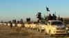 FILE - In this undated file photo released by a militant website, which has been verified and is consistent with other AP reporting, militants of the Islamic State group hold up their weapons and wave its flags on their vehicles in a convoy to Iraq, in Raqqa, Syria. 