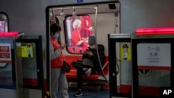 Viajeros con mascarillas leen en sus teléfonos celulares en el Metro de Beijing, 10 de febrero de 2021. El organismo supervisor del internet en China obligará a blogueros e influencers obtengan licencia para publicar opiniones sobre ciertos temas. [AP]