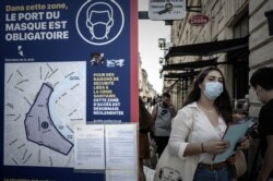 A woman wearing a protective face mask walks past a sign showing the area where wearing a protective mask is mandatory, in Bordeaux, southwestern France, Sept. 16, 2020.