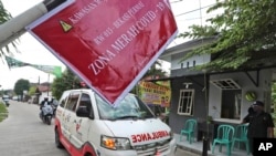 Ambulans yang membawa jenazah korban COVID-19 melaju melewati papan bertuliskan "Zona Merah COVID-19", dalam perjalanan menuju pemakaman untuk dimakamkan, di Bekasi di pinggiran Jakarta, 11 Juli 2021. (AP Photo/Achmad Ibrahim)