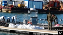 Des garde-côtes tunisiens se tiennent à côté des cadavres de migrants dans le port de Sfax, en Tunisie, le 24 décembre 2020. 