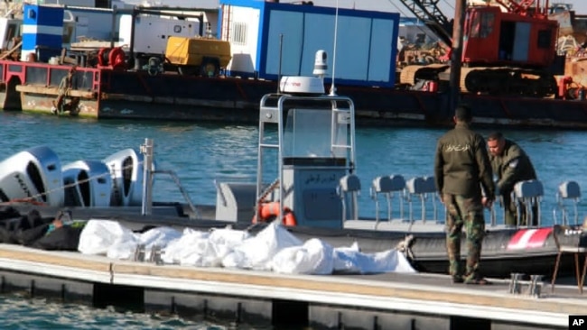 FILE - Tunisian coast guard members stand next to the dead bodies of migrants in the port of Sfax, Tunisia, Dec. 24, 2020.