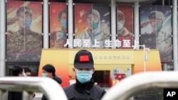 A security officer wearing a mask and a cap with the Chinese national flag guards the entrance after a World Health Organization team's arrival at an exhibition on the fight against the coronavirus, in Wuhan, China, Jan. 30, 2021. 