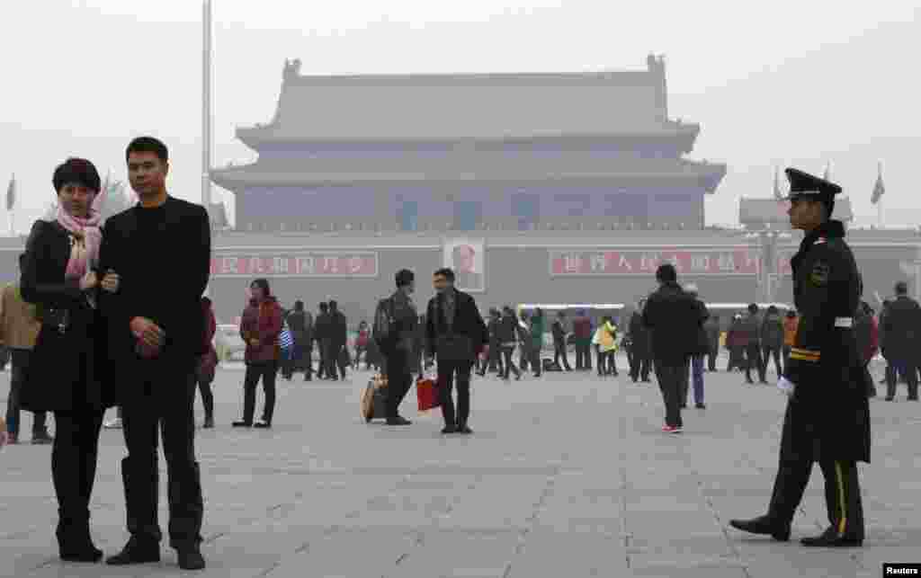 A paramilitary soldier patrols near visitors posing for souvenir pictures at Tiananmen Square, Beijing, China, Nov. 1, 2013. 