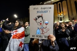 A demonstrator holds a placard depicting a caricature of Bidzina Ivanishvili, billionaire and founder of the ruling Georgian Dream party, with a balloon in the colors of the Russian flag, during an opposition rally in Tbilisi on Oct. 28, 2024.